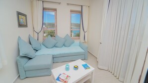 Un salon avec un canapé bleu clair, deux fenêtres avec des rideaux, une table basse blanche et un tableau encadré au mur.