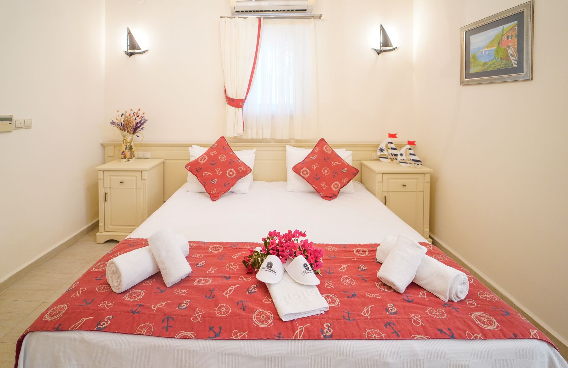 A hotel room with a bed, two nightstands, a window with curtains, a painting on the wall, and a vase with flowers.