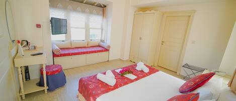 A hotel room with a bed, a window seat, a wardrobe, and a desk with a chair.