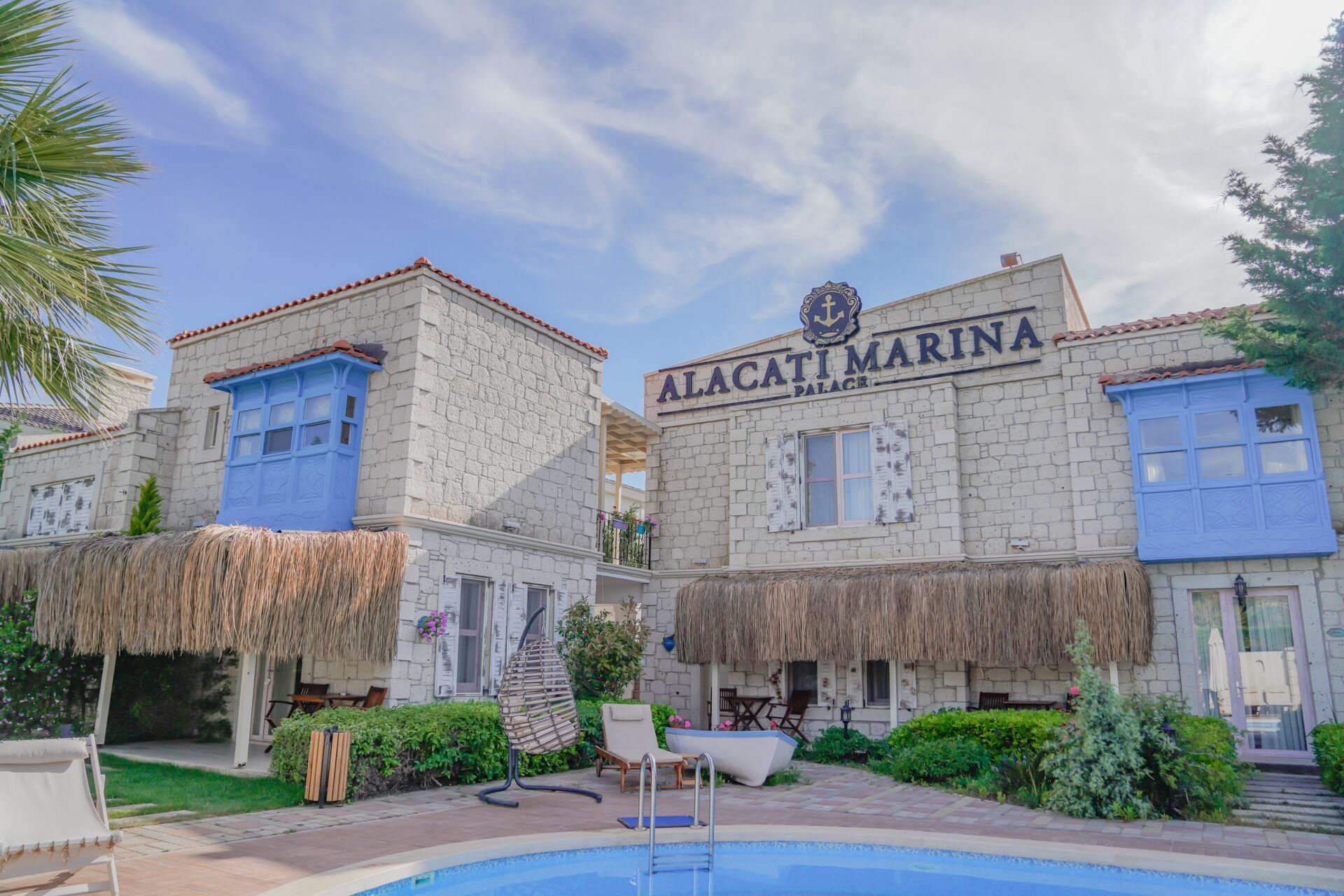 A building with the sign 'Alacati Marina Palace' and a swimming pool in front.