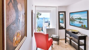 Una habitación con una silla roja, un aparador negro y un cuadro grande de una escena costera.