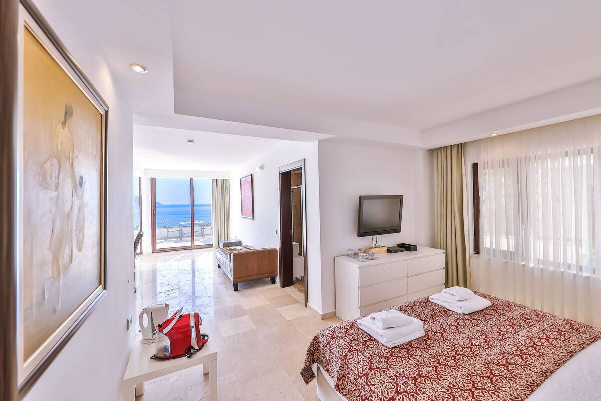 Quarto de hotel com cama, escrivaninha, televisão e vista para o mar.