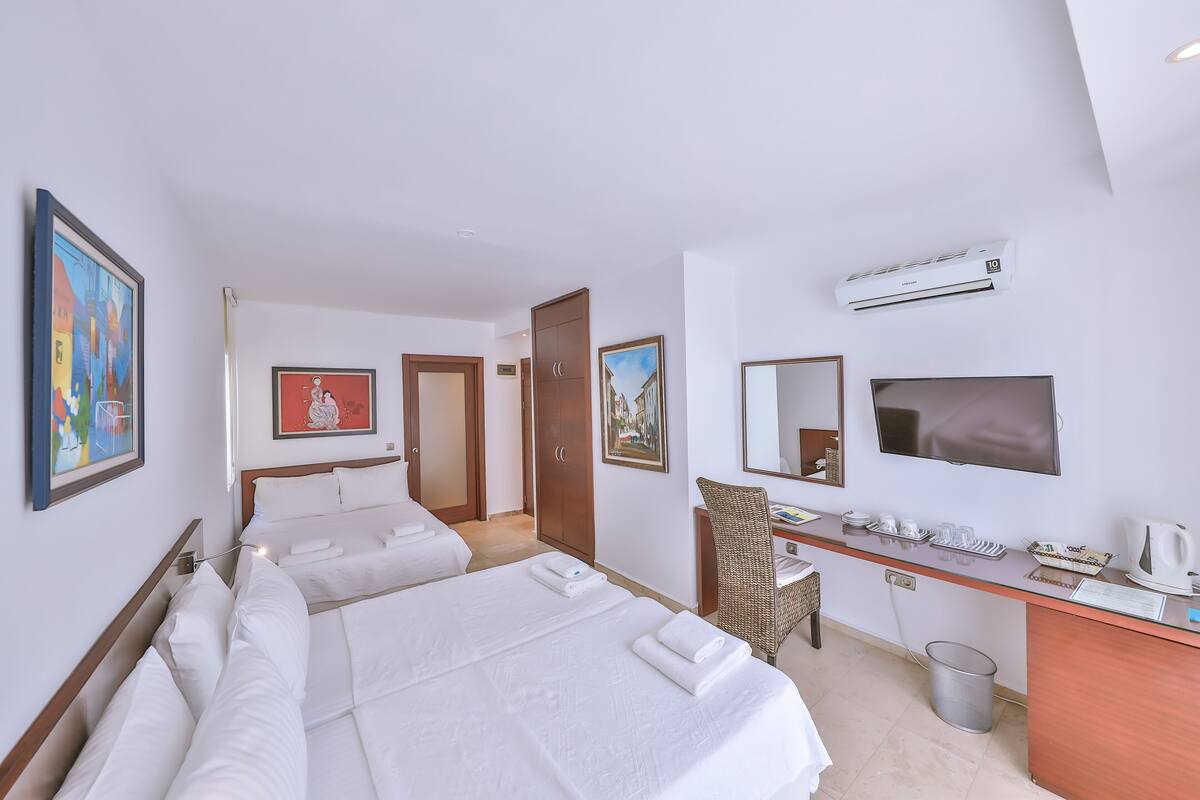 Quarto de hotel com duas camas, uma escrivaninha, uma cadeira, uma televisão e obras de arte nas paredes.
