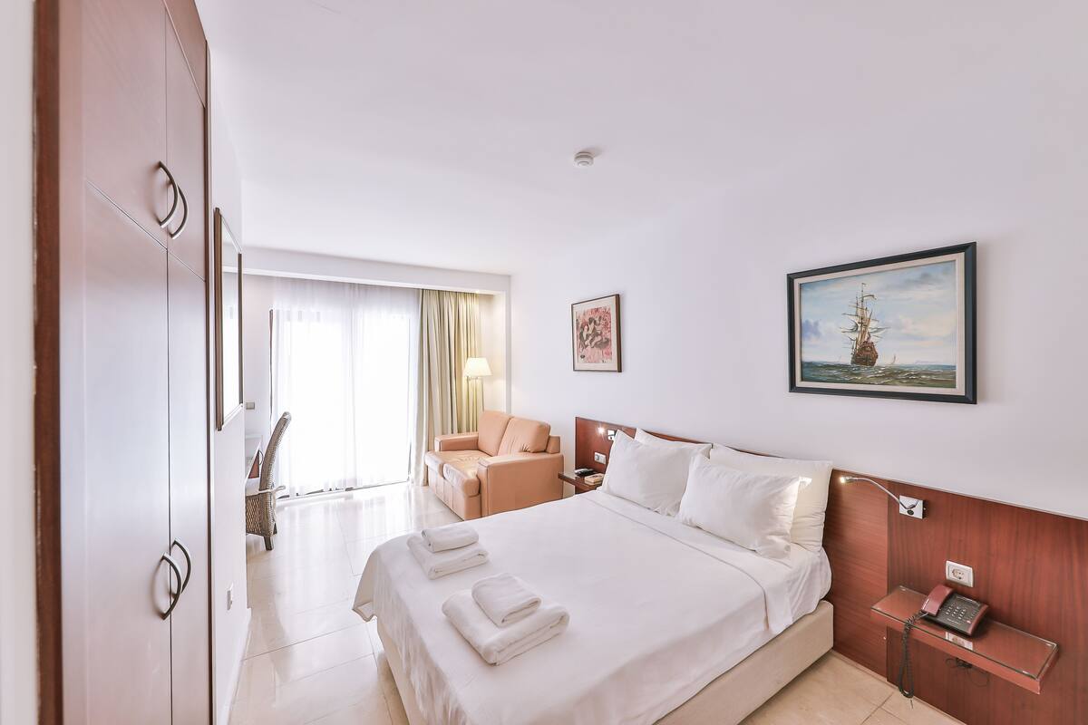 Quarto de hotel com cama grande, escrivaninha, cadeira e um quadro na parede.