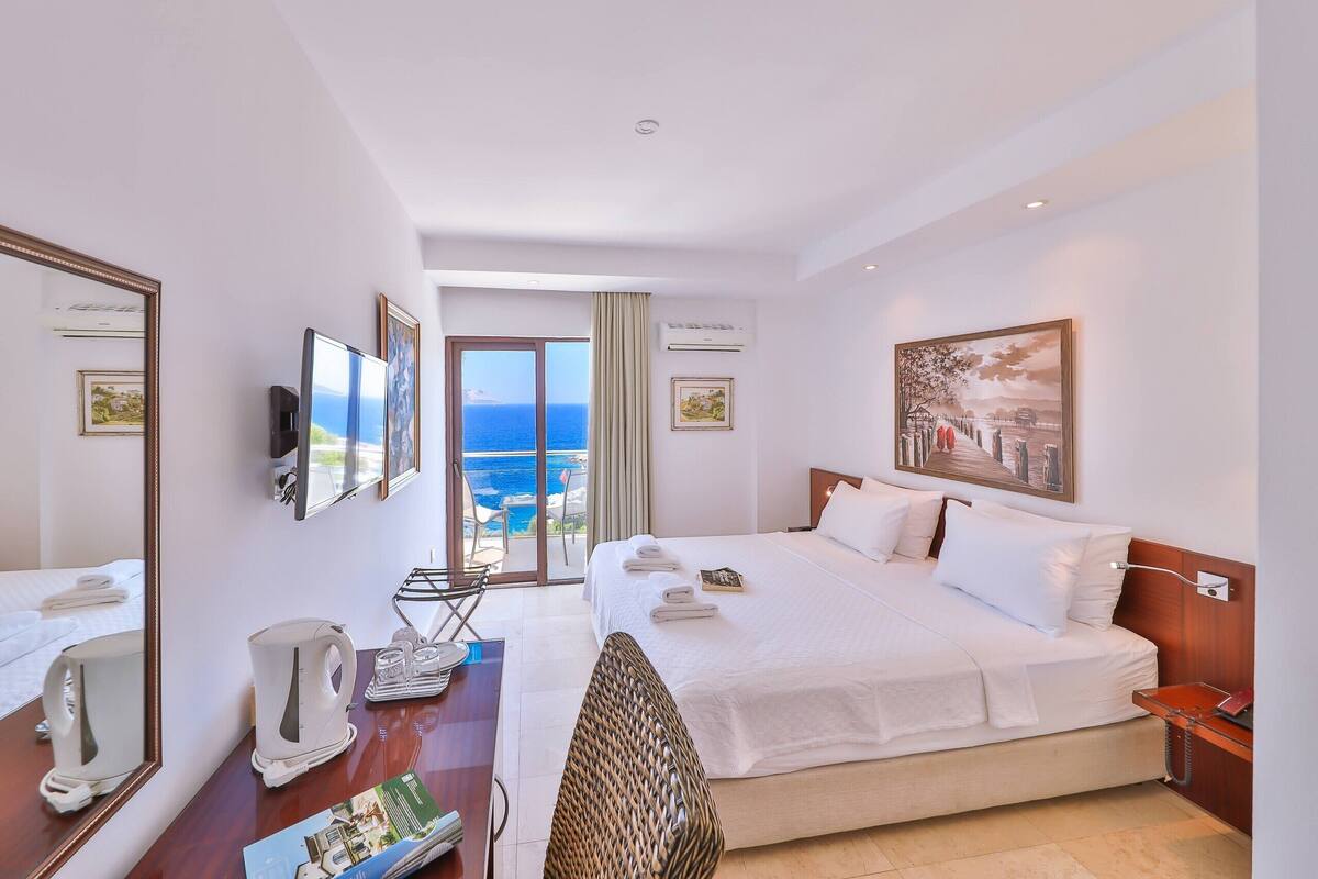 Quarto de hotel com cama, secretária com telefone, cadeira, televisão e janela com vista para o mar.