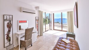Habitación de hotel moderna con escritorio, silla y una cama grande. Varias fotografías enmarcadas adornan las paredes y se aprecia vista al mar a través de amplios ventanales.