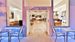 Un interior moderno con un letrero 'GARDENIA', puertas de cristal y vistas a una habitación bien iluminada con un sofá y comedor.