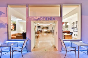 Un interior moderno con un letrero 'GARDENIA', puertas de cristal y vistas a una habitación bien iluminada con un sofá y comedor.