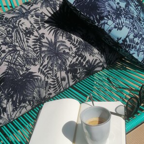 A bed with a tropical leaf pattern, a teal-striped pillow, and a white mug with sunglasses on a table. - Un Hôtel en Ville (La Rochelle)