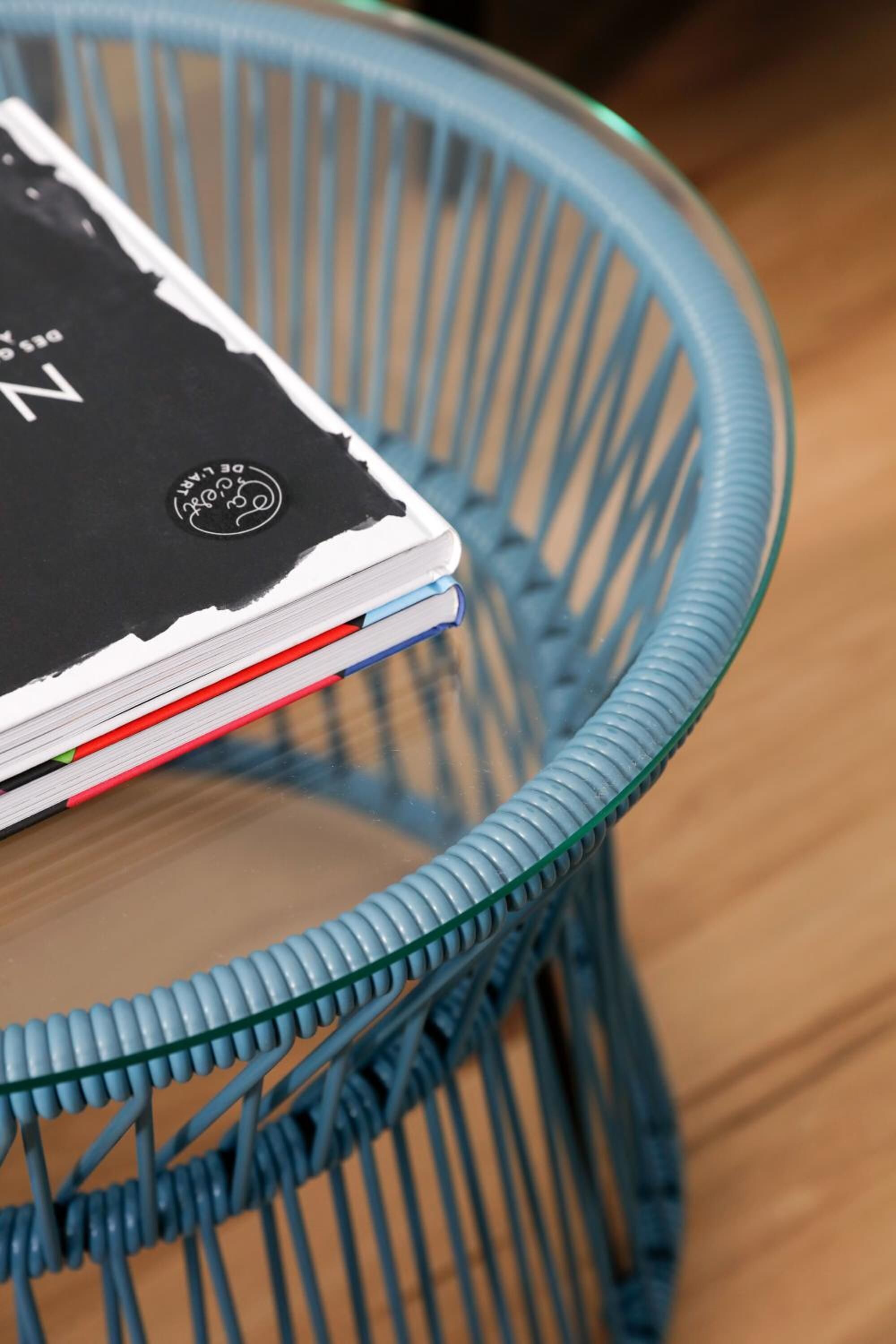 Una pila de cuadernos sobre una mesa de vidrio con estructura de alambre azul.