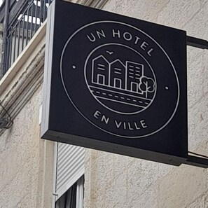 A black sign with a white emblem of a hotel building and the text "UN HOTEL EN VILLE". - Un Hôtel en Ville (La Rochelle)