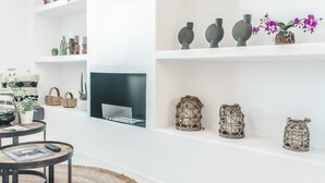 A modern living room with a fireplace, shelves with decorative items, a round table with a remote, and a woven rug.