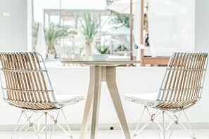 Two wicker chairs with white cushions and a small table with a bowl on it, positioned in front of a large window with a view of palm trees. - Hotel Boutique & Spa Las Mimosas Ibiza (Sant Josep de sa Talaia)