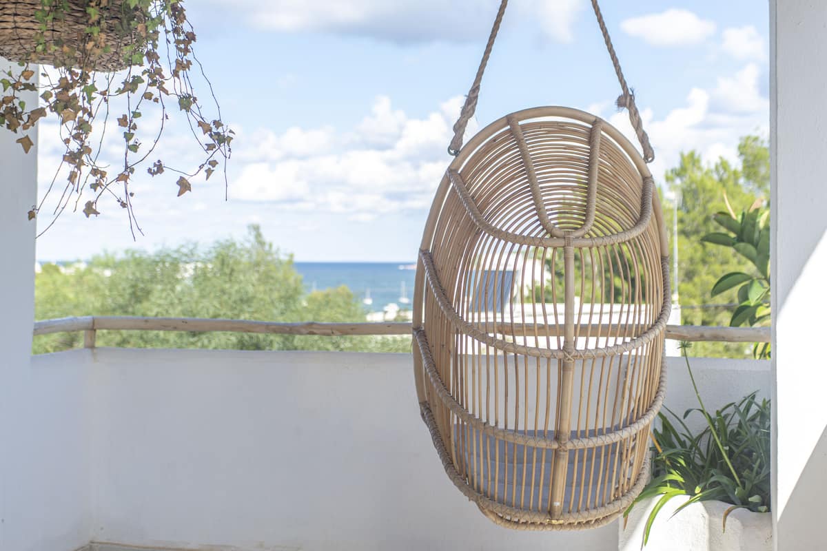 Una silla colgante de mimbre en un balcón con vistas al mar.