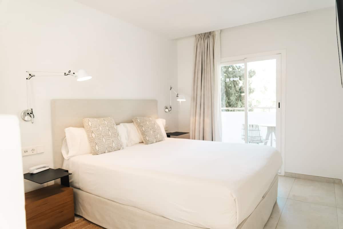 Un dormitorio con una cama grande, mesitas de noche, una lámpara y vistas al exterior.