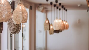 A restaurant interior with wicker furniture, hanging pendant lights, and a glass partition.