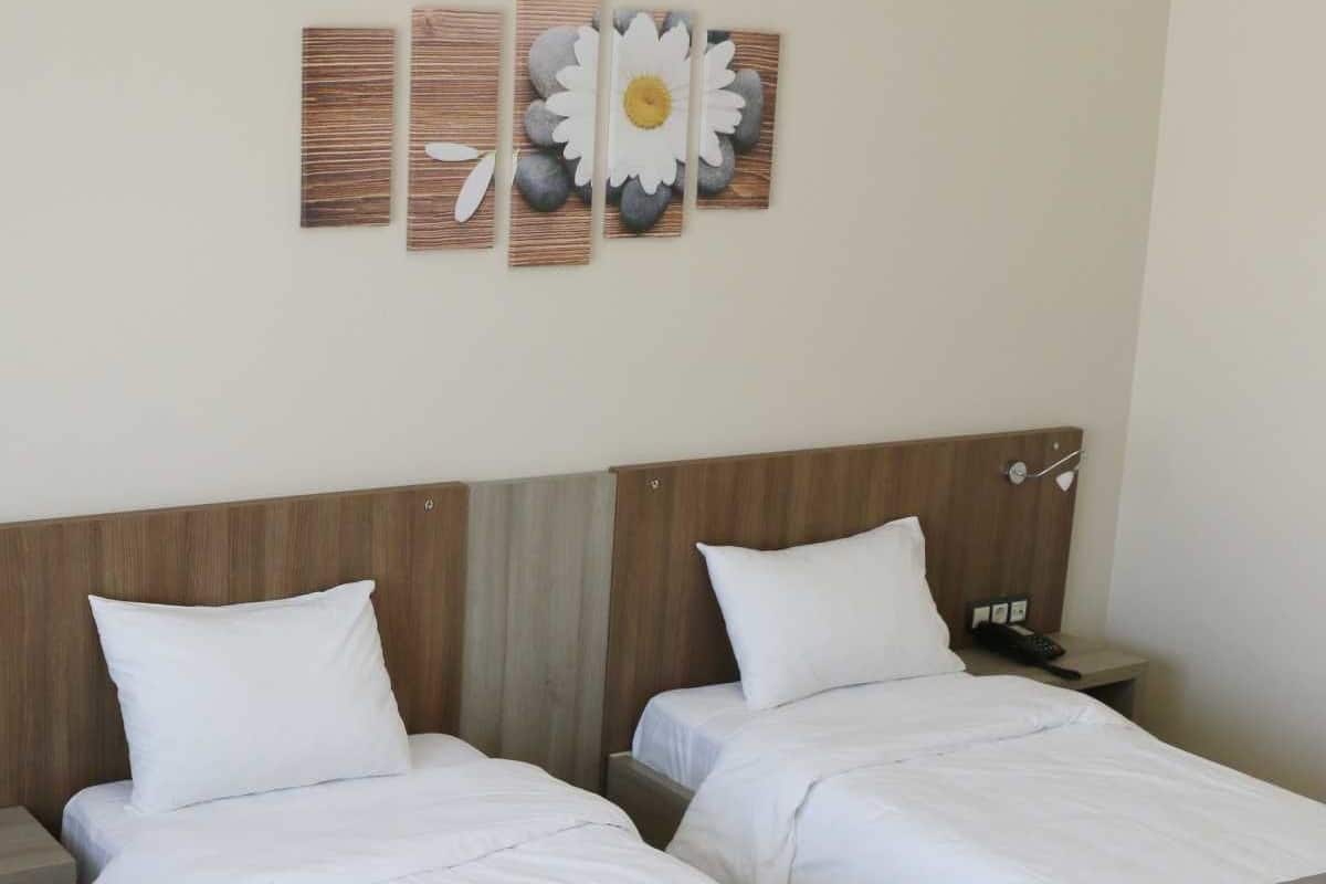 A hotel room with two single beds, wooden headboards, white bedding, a nightstand with a phone, and a wall art piece above the beds.