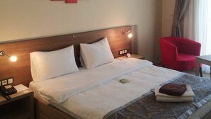 Habitación de hotel con cama, mesita de noche con teléfono, una silla roja y una obra de arte en la pared.