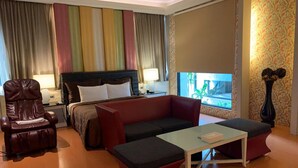 A hotel room with a bed, a red sofa, a small table, a leather armchair, a nightstand with a lamp, and a window with curtains. - Leedon Motel (Kaohsiung)