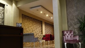 A reception area with a wooden desk, a seating area with red and grey upholstered chairs, and a large potted plant.