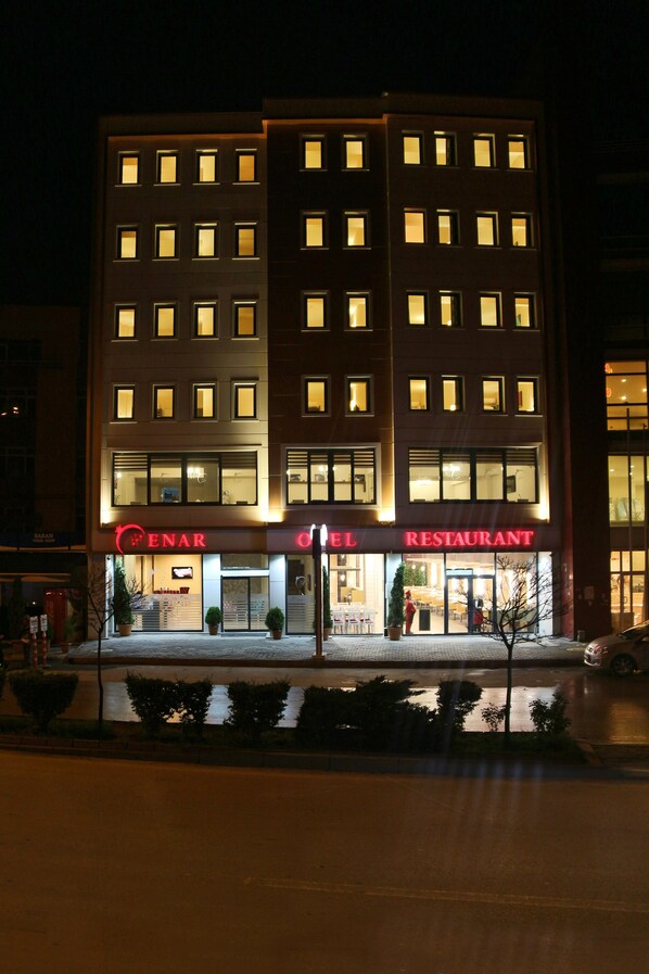 Un hotel con restaurante en la planta baja, varios pisos y una fachada bien iluminada.