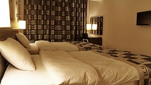 A hotel room with a large bed, two bedside tables with lamps, a TV on the wall, and patterned curtains.