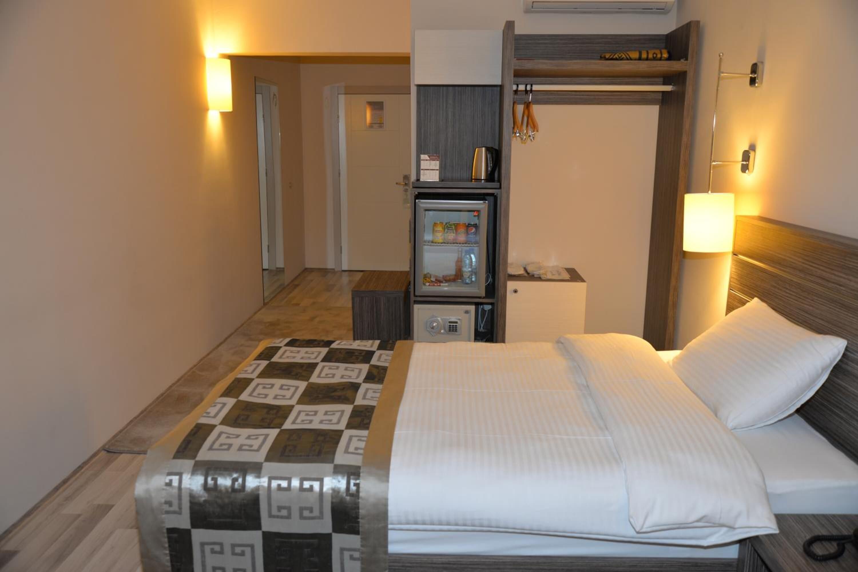 A hotel room with a bed, a small refrigerator, a microwave, a bedside table, and a lamp.