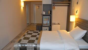 A hotel room with a bed, a small refrigerator, a microwave, a bedside table, and a lamp.