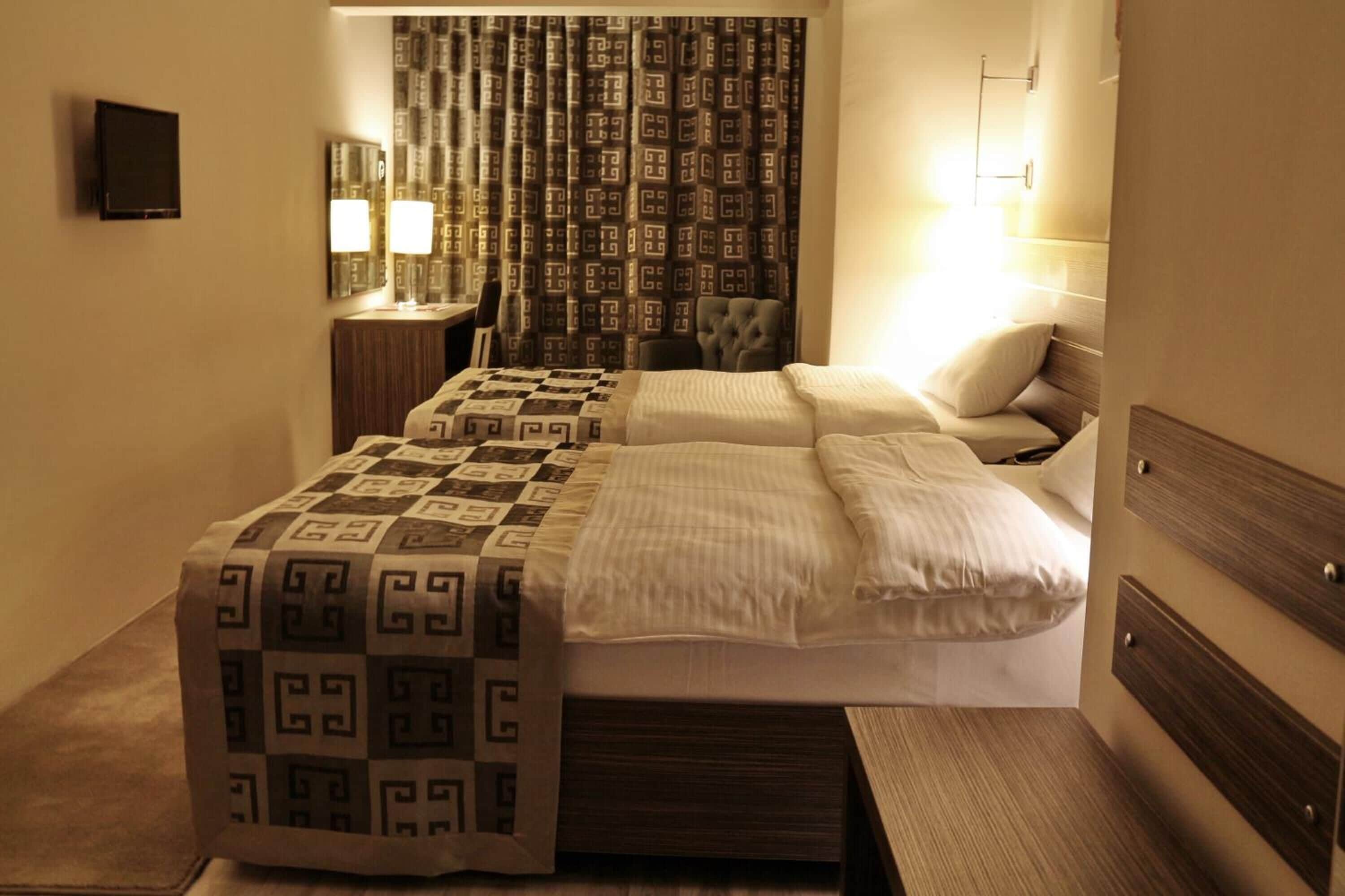 Una habitación de hotel con cama, mesita de noche, lámpara y cortinas.