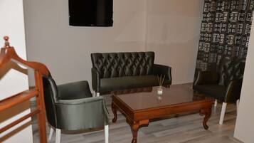 Un salon avec une table basse en bois, deux canapés en cuir noir et un téléviseur fixé au mur.