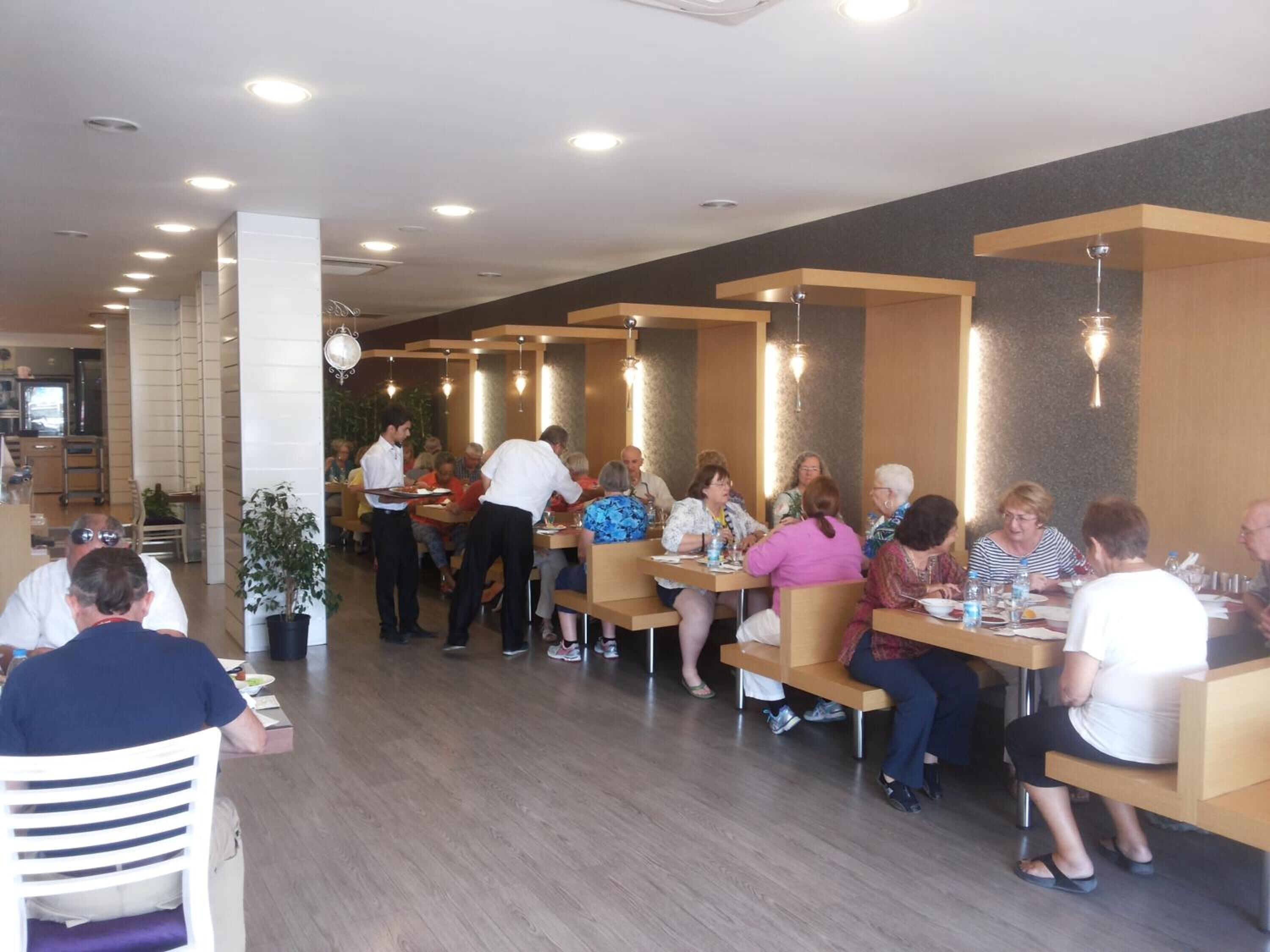 A restaurant with wooden tables and chairs, a waiter serving food, and a modern interior design.