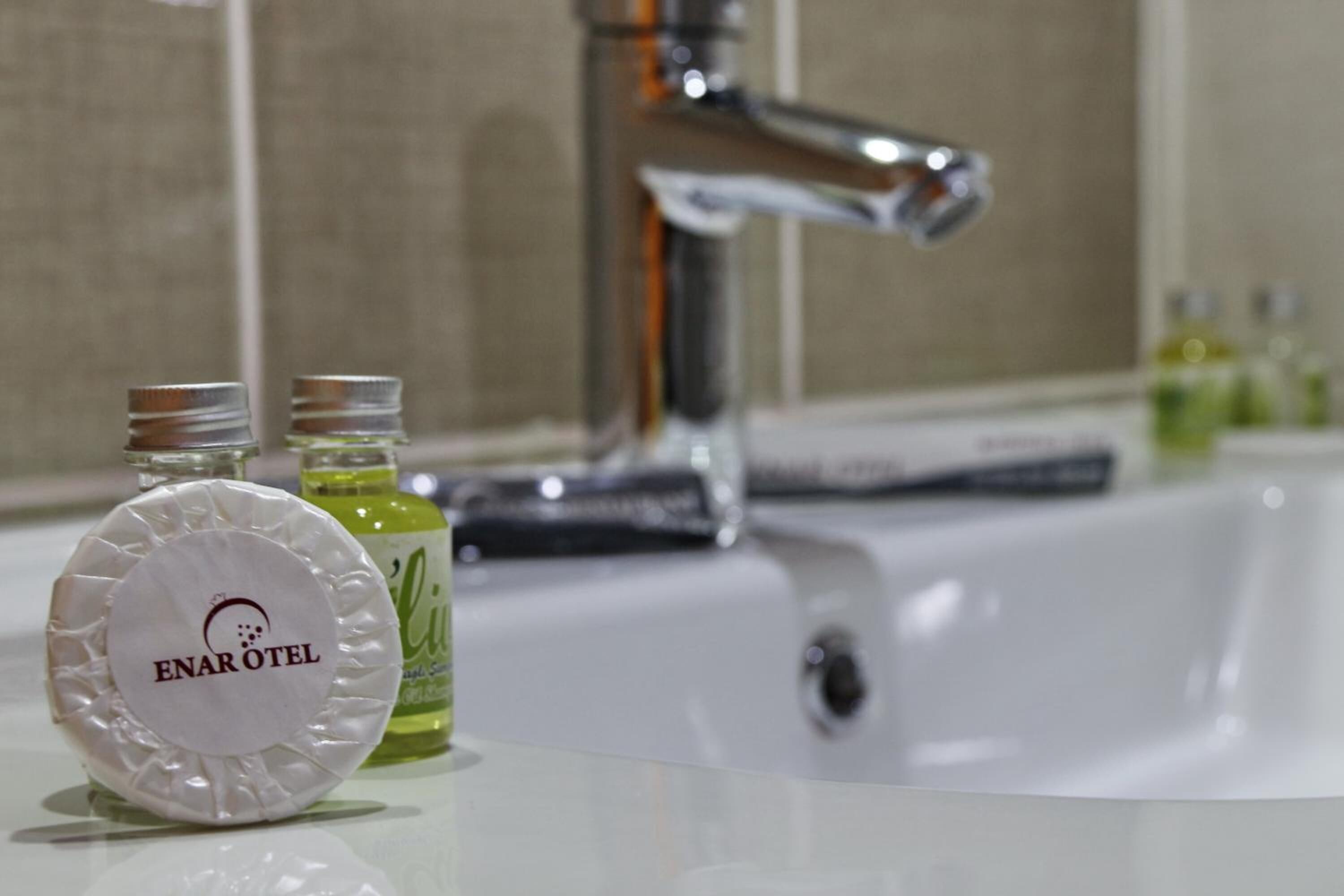 Un baño con un lavabo blanco, un grifo cromado y dos botellas de jabón Enarotel sobre la encimera.