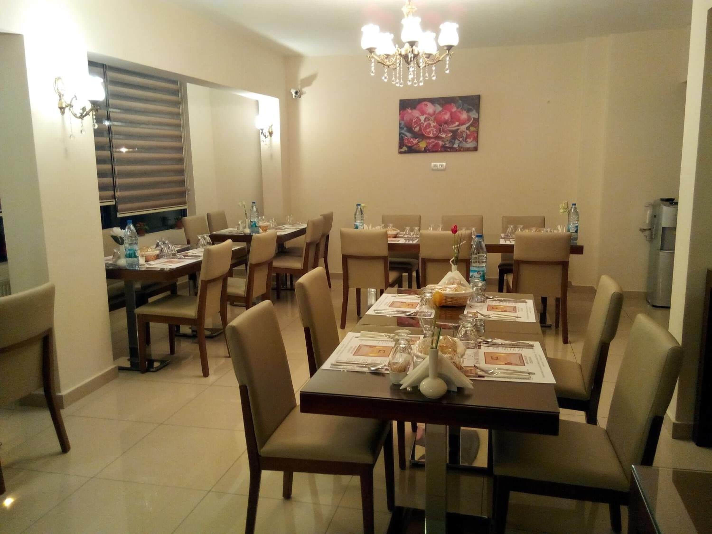A dining area with multiple tables set for a meal, chairs, a chandelier, and a wall-mounted painting.