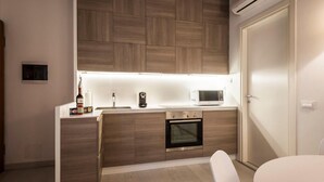 A compact kitchen with wooden cabinetry, a built-in oven, a microwave, and a small countertop with a bottle and a container. - MYSWEETPLACE - Santa Maria Formosa Apartment (Venice)