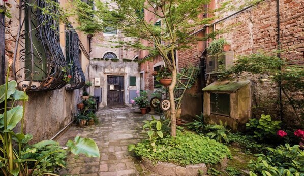 Stroll through this charming alleyway, lined with lush potted plants and brick walls, leading to a welcoming entrance.