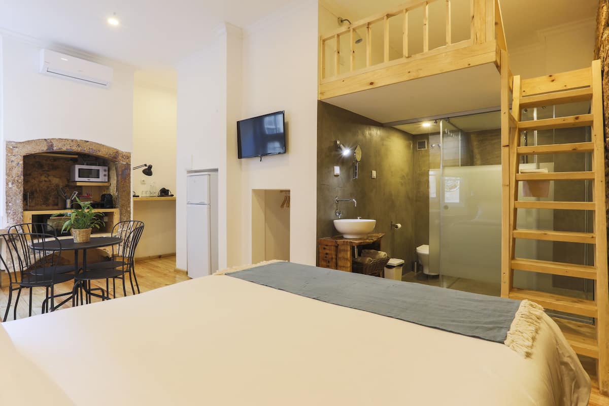 Una habitación compacta con cama, zona de comedor con mesa y sillas, cocina con microondas y baño con lavamanos y ducha.