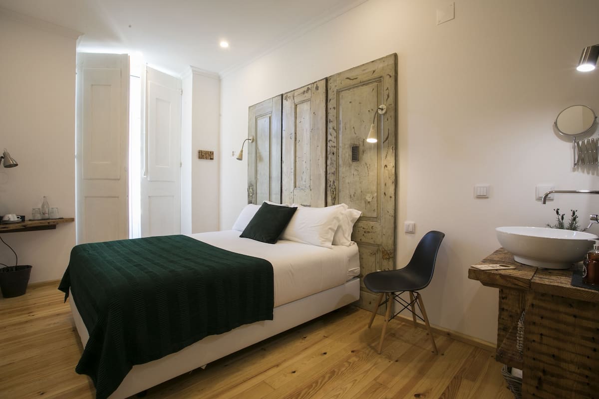 Un dormitorio con cama, una silla, un aparador de madera y un baño con lavabo y espejo.