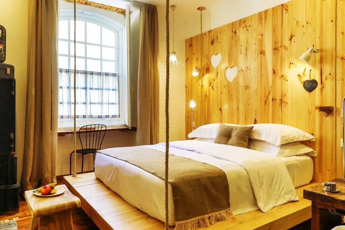 A cozy bedroom with a wooden headboard, a bed with white linens, a bedside table with a lamp, and a window with curtains.