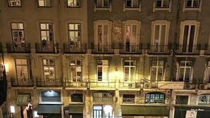 Un edificio de varios pisos con una entrada central, balcones y una tienda en la planta baja.