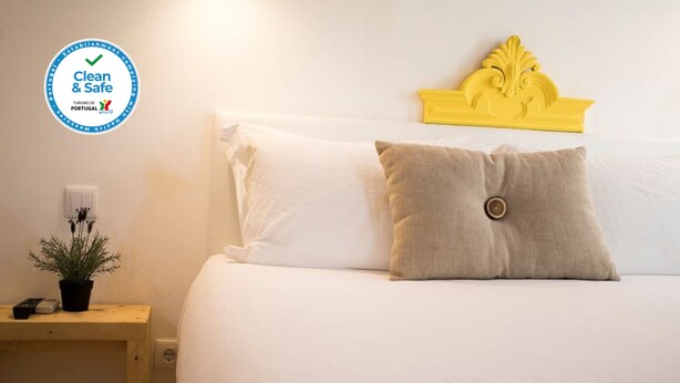 Habitación de hotel limpia y segura con una cama bien hecha, una mesita de noche pequeña con una planta y un cabecero decorativo.