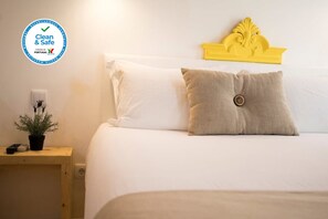 A clean and safe hotel room with a neatly made bed, a small bedside table with a plant, and a decorative headboard.