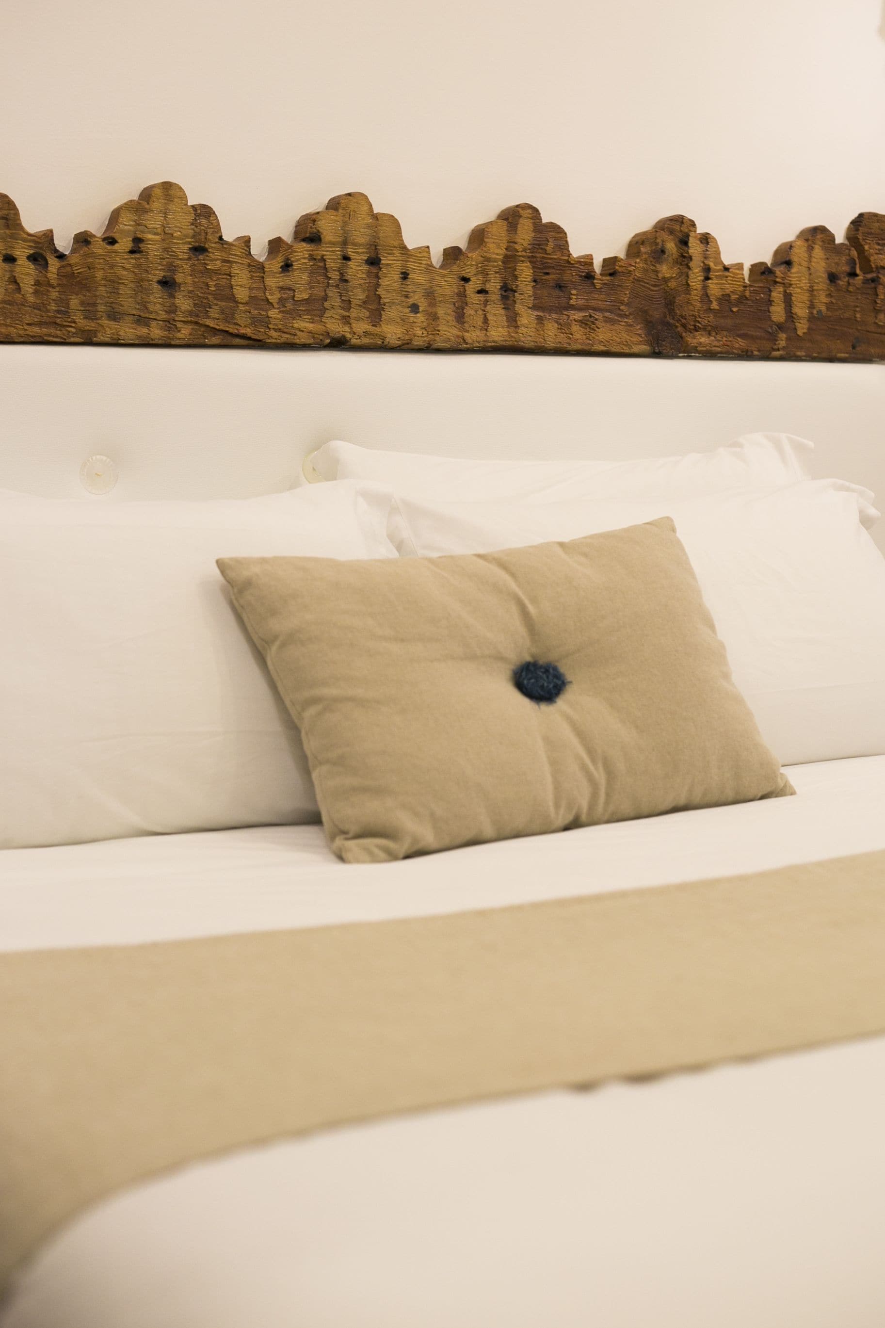 A bed with white bedding and a beige pillow.