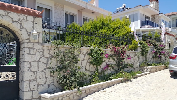 A stone wall with climbing plants and flowers, a metal gate, and a parked car.