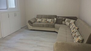 A living room with a beige sofa, patterned cushions, a wooden cabinet, and a window.