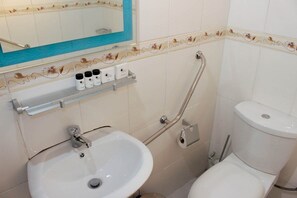 Un baño con lavamanos, inodoro y estante con artículos de aseo.