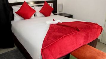 Una cama bien hecha con ropa de cama blanca y roja, un plaid rojo y una almohada a juego en rojo.