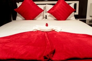 Una cama bien hecha con una colcha y almohadas rojas, un cabecero blanco y una pared de fondo blanca.
