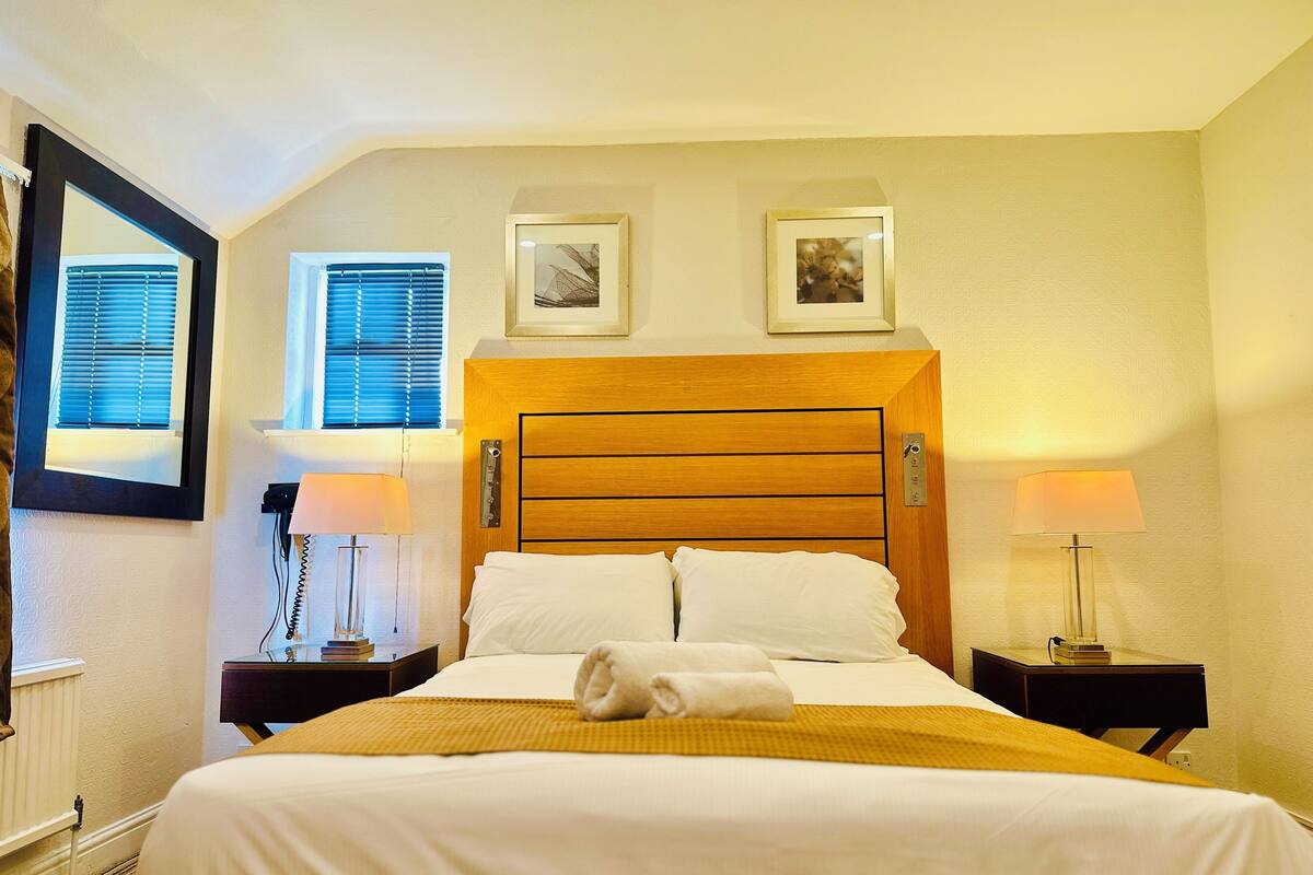 A neatly made bed with a wooden headboard, two bedside tables with lamps, and framed pictures on the wall.