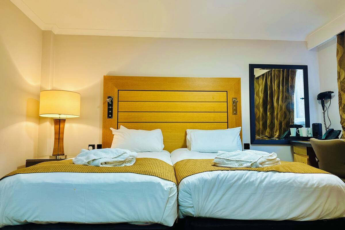 A hotel room with a double bed, a bedside table with a lamp, a hairdryer, and a mirror.