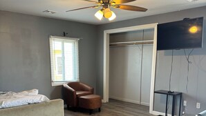 A bedroom with a bed, a chair, a ceiling fan, a TV, and a walk-in closet. - 12 Ashworth Ave (Hampton)